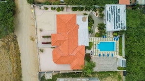 An aerial view of a property with a swimming pool, a large covered patio, and a parking area.