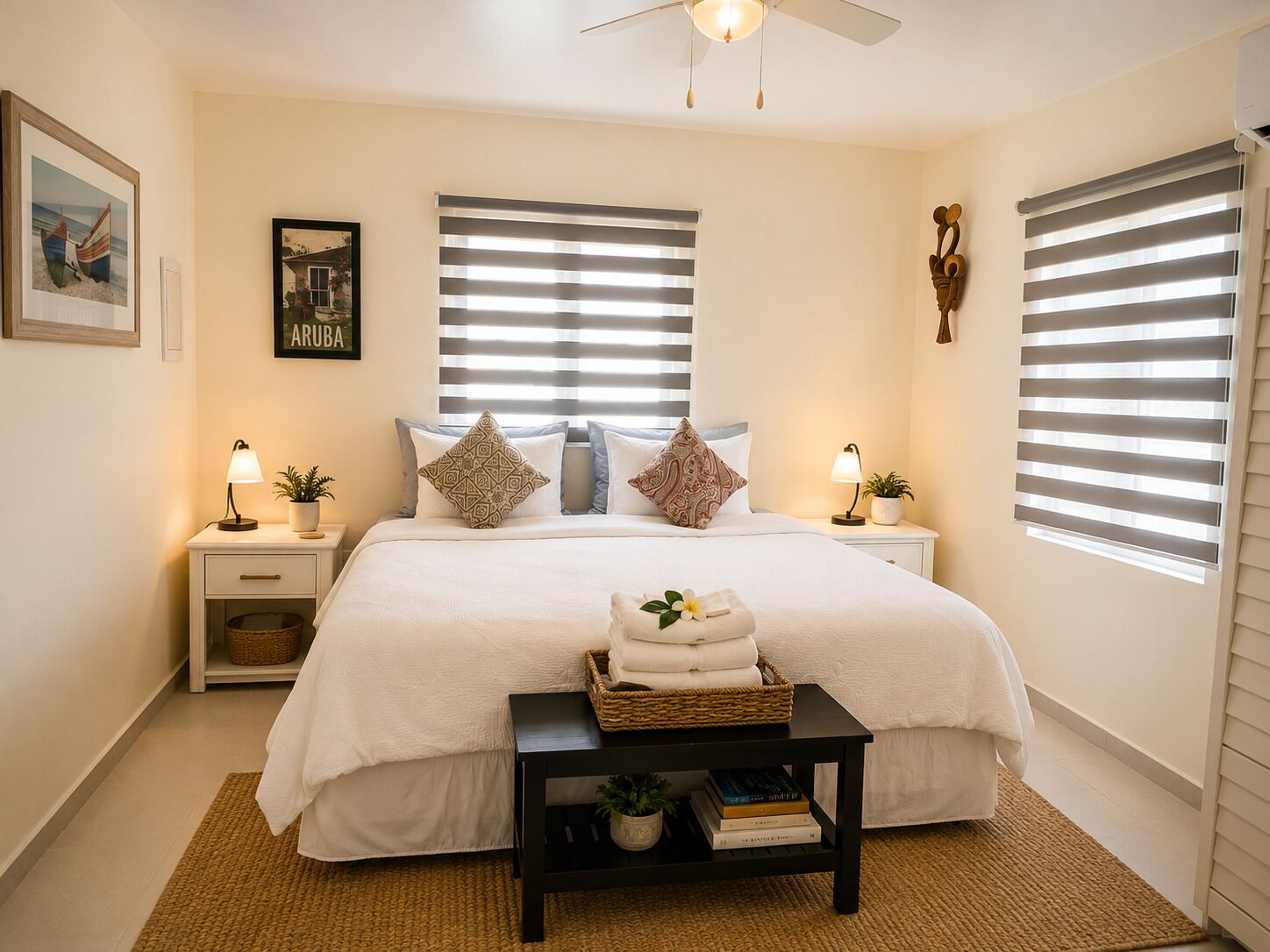 Une chambre à coucher comprenant un lit, deux tables de chevet, une commode, un ventilateur de plafond et une fenêtre avec des stores.