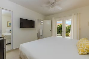 A bedroom with a bed, a TV, a ceiling fan, and a view of the outdoors.