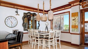 A dining area with a round table, white chairs, a clock, and hanging light fixtures.