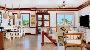 A spacious living room with a high ceiling fan, a dining area with white chairs, a sofa with a view, and a television on the right.