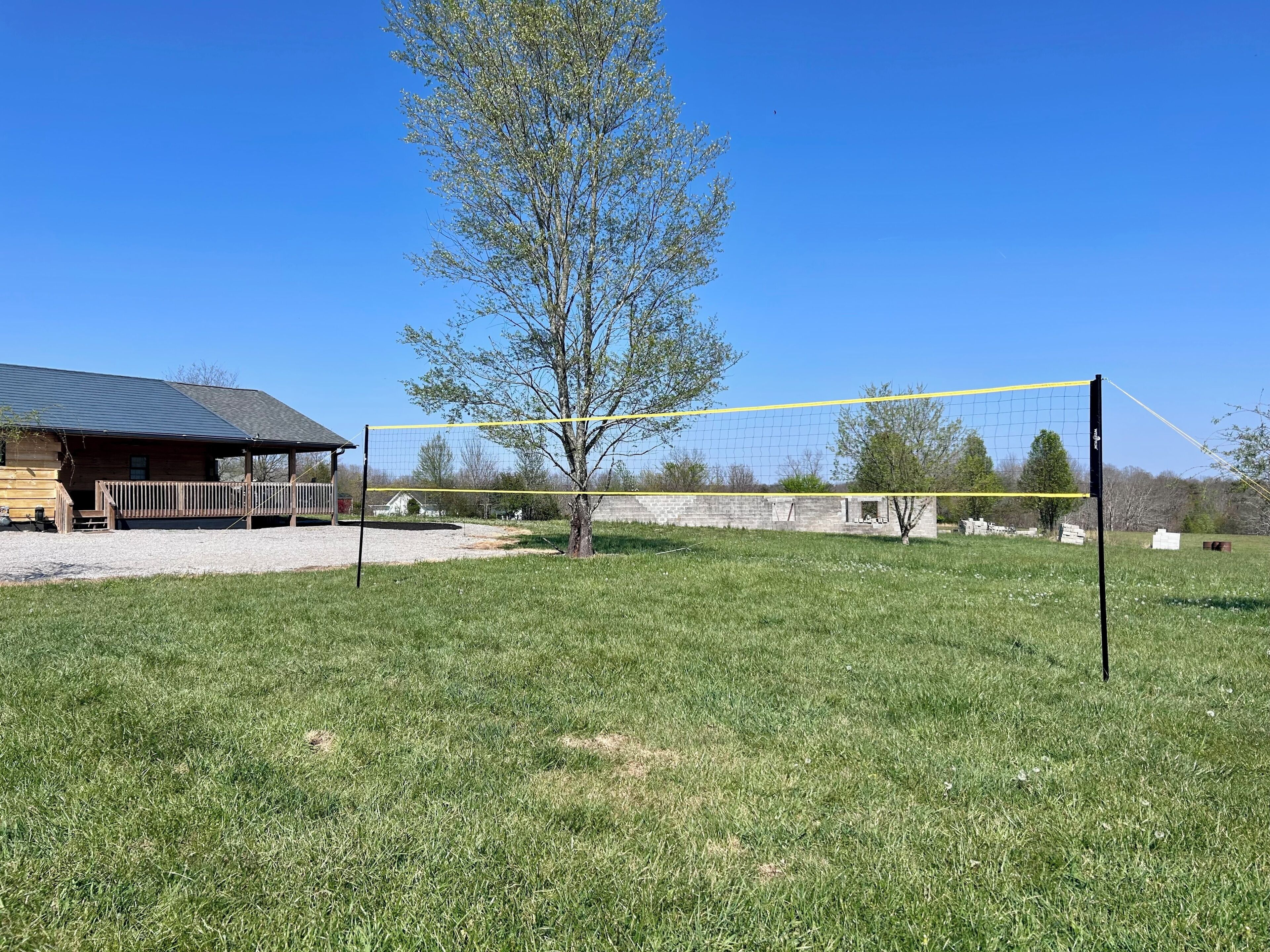Een volleybalnet in een grasveld met een houten hutje op de achtergrond.