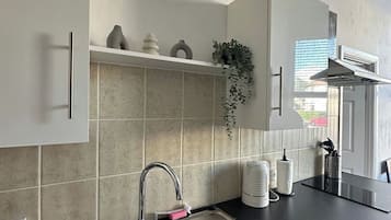 A kitchen with a stainless steel sink, white cabinets, a black countertop, and a window with blinds.