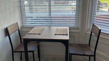 A dining area with a table and four chairs, large windows with blinds, and a view of the outside.
