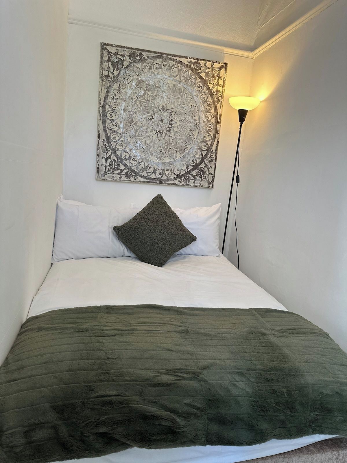 A bed with a green blanket, white pillows, and a decorative wall piece above it.