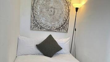 A bed with a green blanket, white pillows, and a decorative wall piece above it.