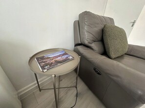 A modern living room with a leather sofa, a round table with a magazine, and a cable on the floor.