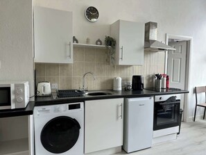A compact kitchen with a washing machine, microwave, toaster, and oven.