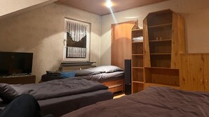 Ein Schlafzimmer mit zwei Betten, einem Holzschrank, einem Fenster mit Vorhängen und einer Deckenleuchte.