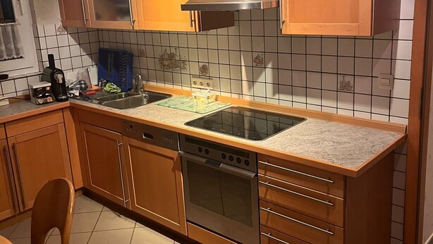 Eine Küche mit Holzschränken, einer Edelstahl-Dunstabzugshaube, einem eingebauten Geschirrspüler und einer gefliesten Rückwand.