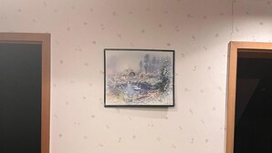 Ein Zimmer mit einem Holzschrank, einem gerahmten Bild an der Wand und Tapete mit Muster.