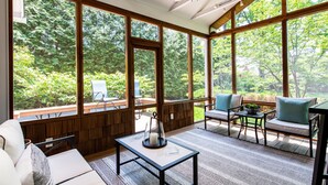 Een zonnehuis met grote ramen, een plafondventilator en een zithoek met een tafel en stoelen.