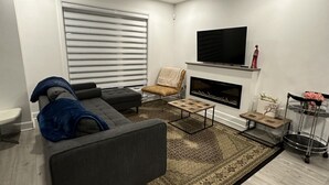 A modern living room with a grey sofa, a small armchair, a coffee table, a fireplace, and a TV mounted on the wall. - Beautiful House in mont tremblant,ski hills,

You will feel like you’re at home. (Mont-Tremblant)