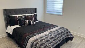 A bedroom with a tufted headboard, a bed with a patterned bedspread, multiple pillows, and a window with blinds. - Beautiful House in mont tremblant,ski hills,

You will feel like you’re at home. (Mont-Tremblant)