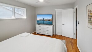 Un dormitorio con una cama, un televisor sobre una cómoda, un ventilador de techo y una puerta.