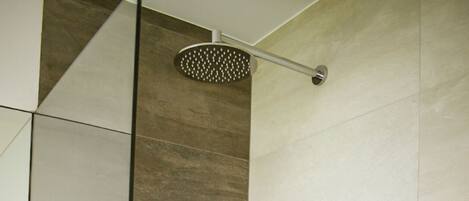 A modern bathroom with a glass shower enclosure, a handheld showerhead, a wall-mounted faucet, and a yellow towel on the wall.