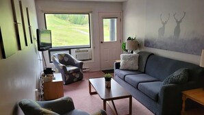 A living room with a sofa, armchair, coffee table, and a TV on a stand. - Griz Inn Condo on the Hill - 100 steps from lift (Fernie)