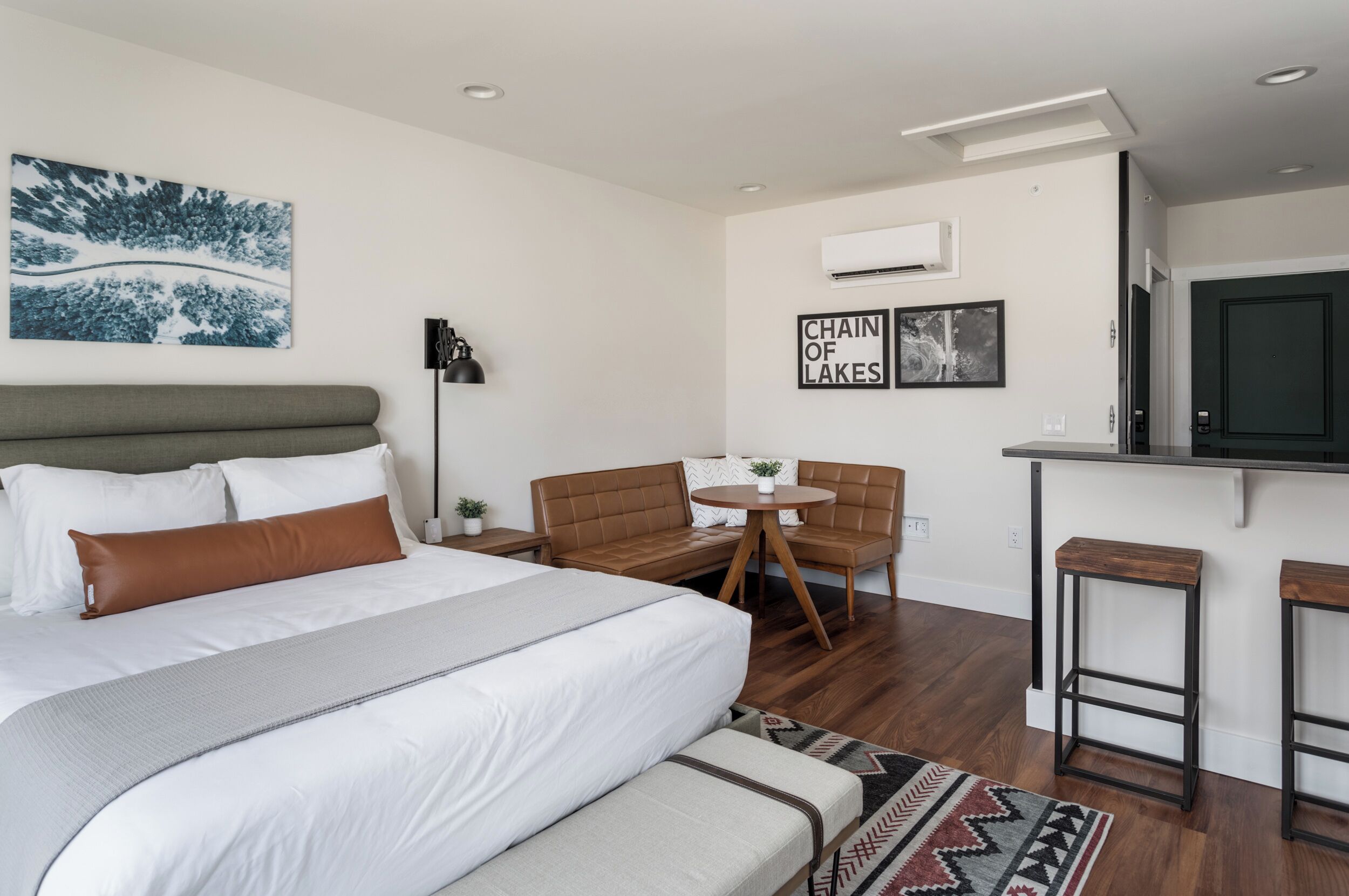 A modern hotel room with a large bed, a seating area with a table, and a kitchenette.
