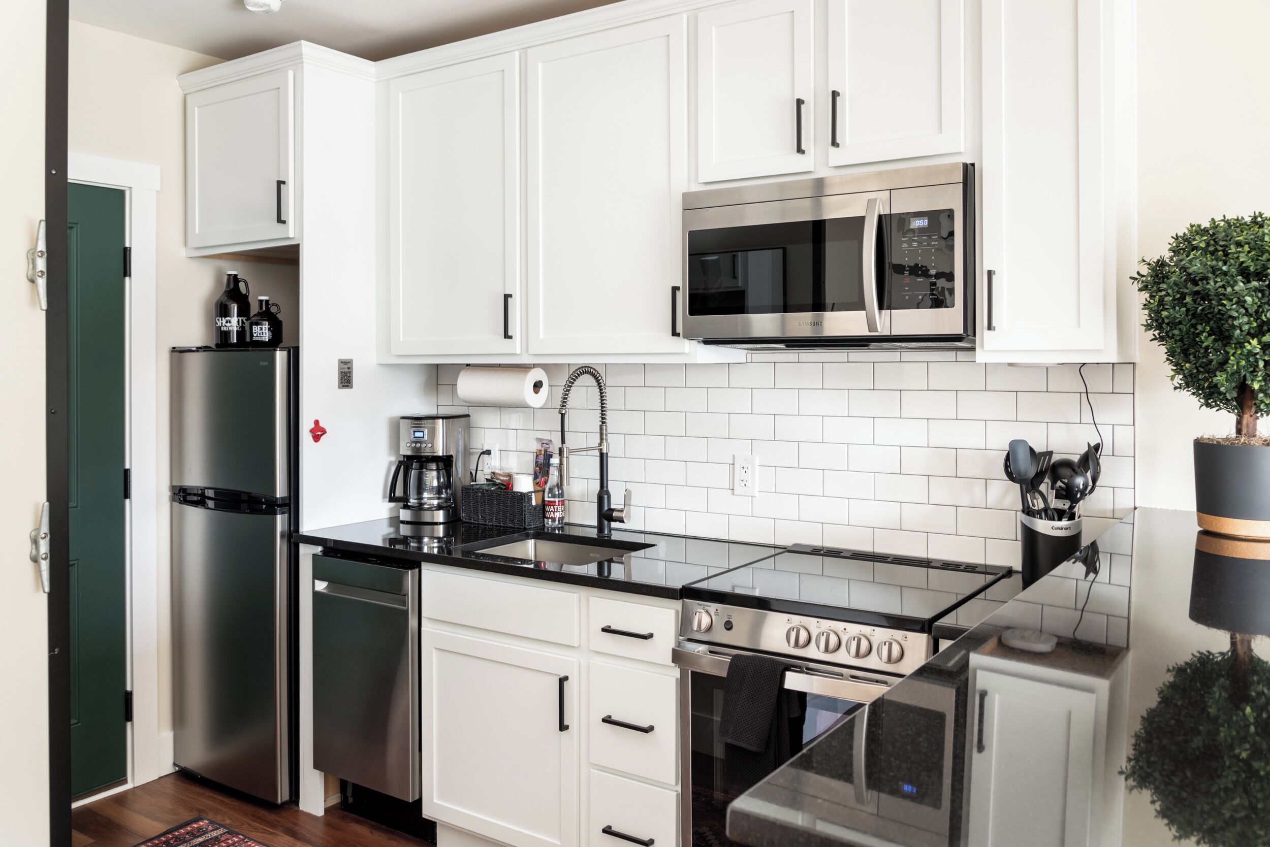 A modern kitchen with white cabinets, stainless steel appliances, a black countertop, and a small potted plant.