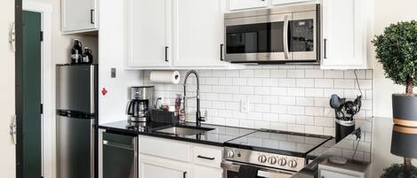 A modern kitchen with white cabinets, stainless steel appliances, a black countertop, and a small potted plant.