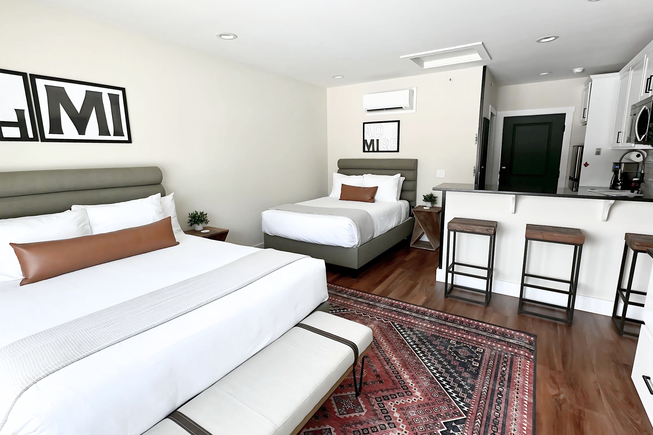 Een moderne hotelkamer met een groot bed, een kleiner bed, een kitchenette en een barhoek.