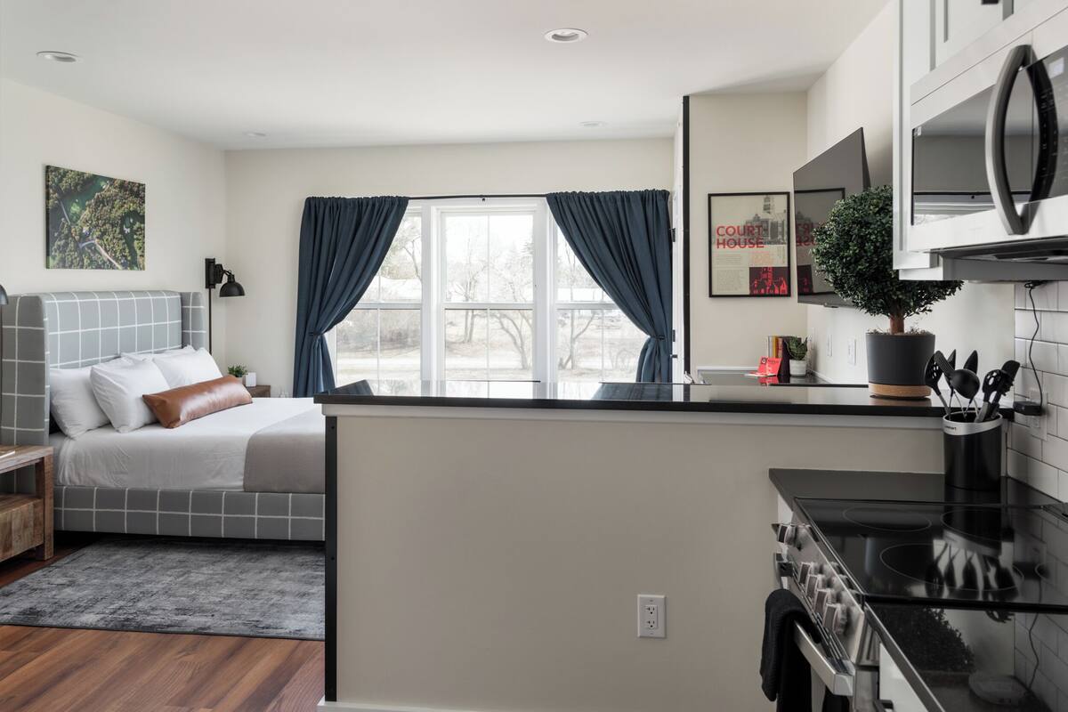 A modern bedroom with a bed, bedside table, and a view of the outdoors through a window.