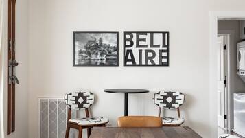 Un comedor con una mesa de madera, dos sillas con cojines estampados, una mesita redonda y dos cuadros en la pared.