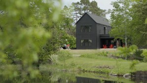 A modern two-story house with a dark exterior, surrounded by lush greenery and a small pond. - Spillway Lodges (Bellaire)