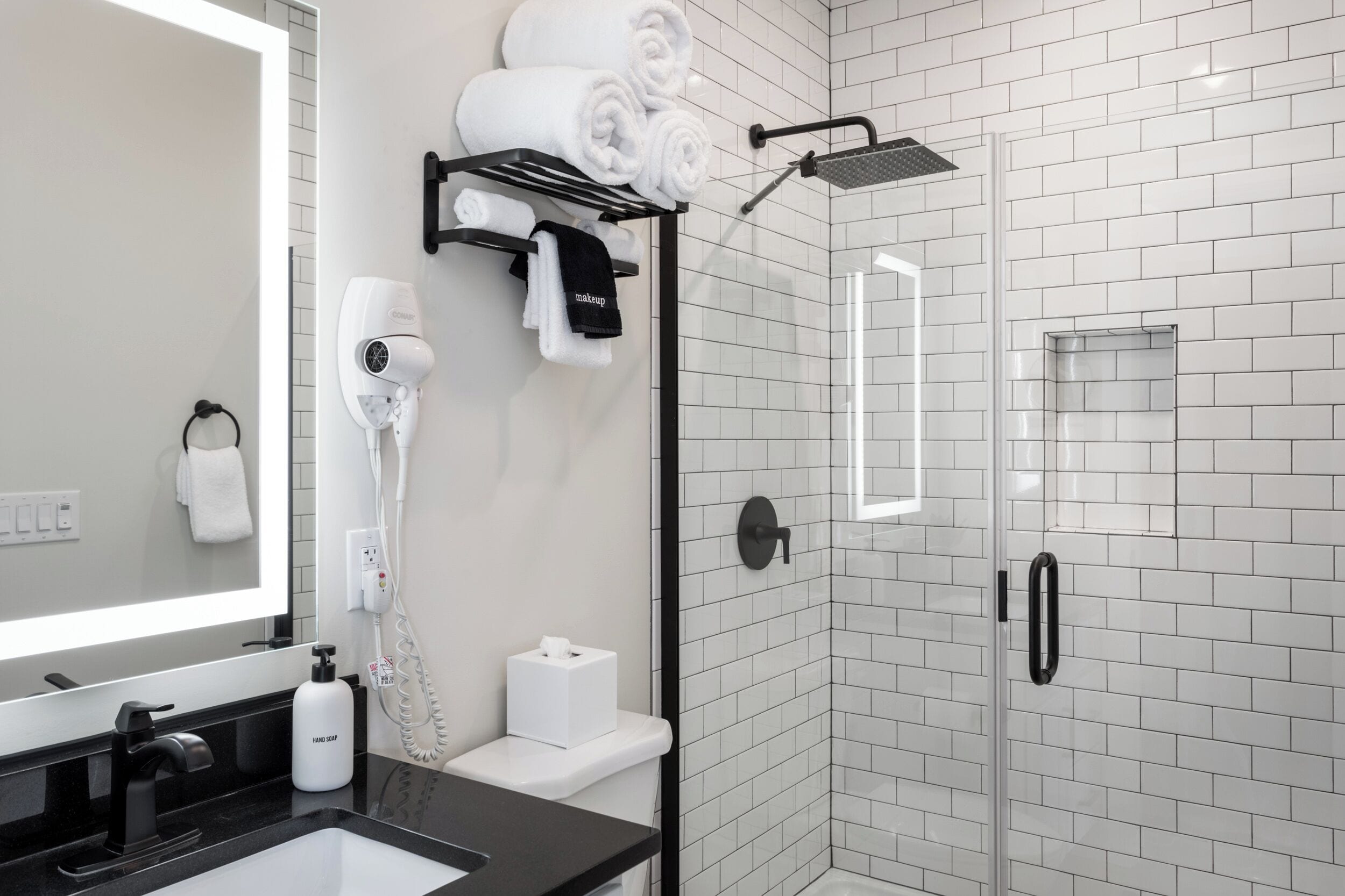 A modern bathroom with a black sink, white tiles, a glass shower enclosure, and a towel rack with neatly folded towels.
