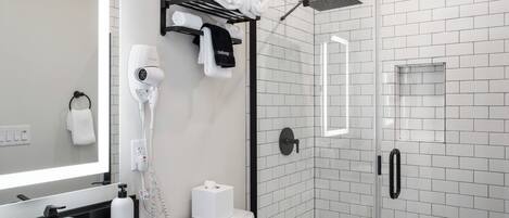 A modern bathroom with a black sink, white tiles, a glass shower enclosure, and a towel rack with neatly folded towels.