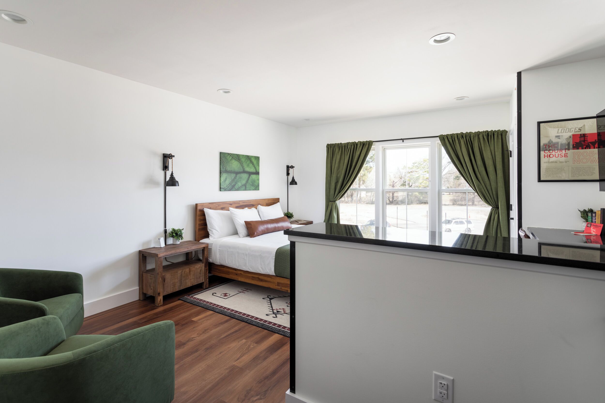 Un dormitorio moderno con una cama de madera, un sofá verde, una mesita de noche pequeña de madera y un ventanal con cortinas.