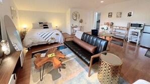 A modern, well-lit living room with a sofa, a coffee table, and a dining area with a microwave and kettle.