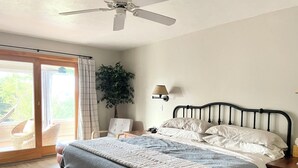 Un dormitorio con cama, banco, ventilador de techo y vistas al exterior.