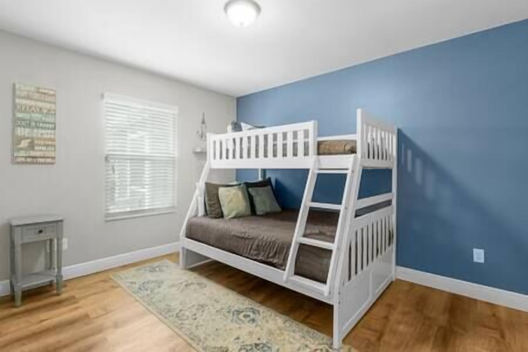 A bunk bed room with a blue wall, a wooden floor, and a small table.