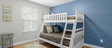 A bunk bed room with a blue wall, a wooden floor, and a small table.