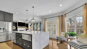 A modern kitchen with a marble island, stainless steel appliances, and a dining area with a striped bench and potted plant. - Serene Farms Hot Tub Pool Sunroom on 7 Acres (Hiram)