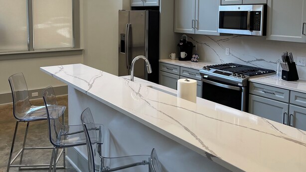 A modern kitchen with a marble countertop, stainless steel appliances, and clear chairs. - Sleek & Sophisticated: Modern Luxe in the Heart of New Orleans (New Orleans)