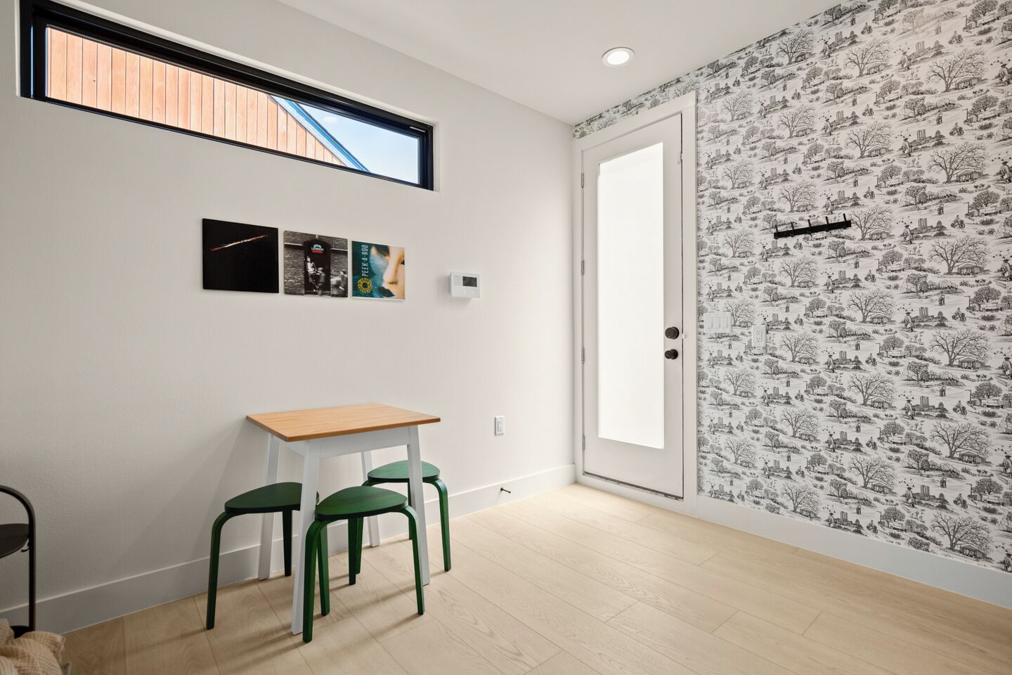 A room with a wooden table, two green chairs, a white door, and a window with a view of a wooden structure.