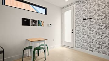 A room with a wooden table, two green chairs, a white door, and a window with a view of a wooden structure.