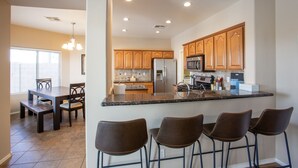 A modern kitchen with wooden cabinets, a central island with bar stools, and a dining area with a table and chairs. - Newly Remodeled Beautiful Home and Large Sparkling Pool, New Hot Tub & Game Room (San Tan Valley)