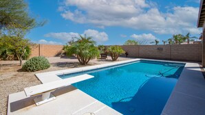 A rectangular swimming pool with a clear blue water surface, surrounded by a brick wall and various plants. - Newly Remodeled Beautiful Home and Large Sparkling Pool, New Hot Tub & Game Room (San Tan Valley)