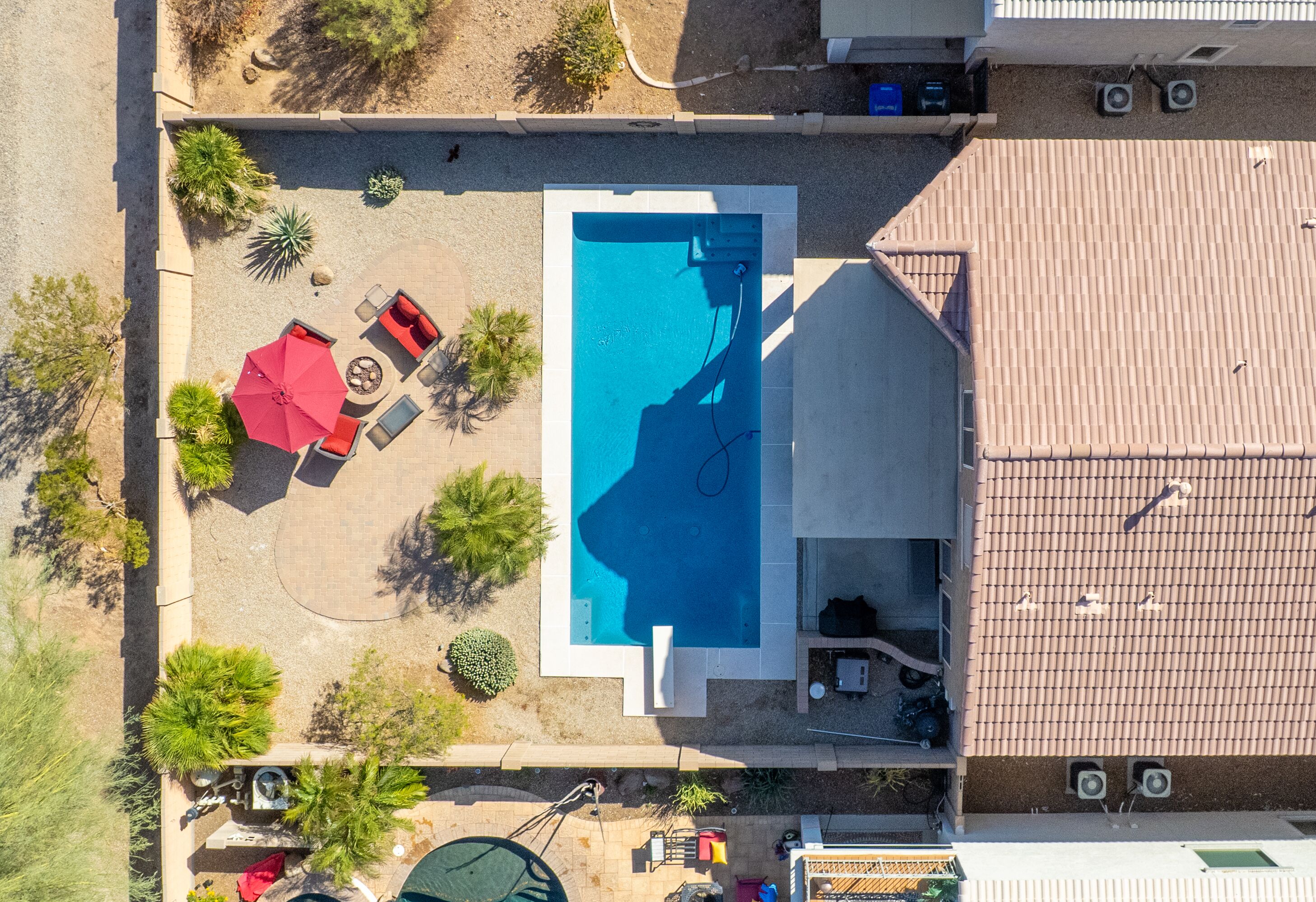 An aerial view of a residential property with a swimming pool, patio furniture, and a covered outdoor seating area.