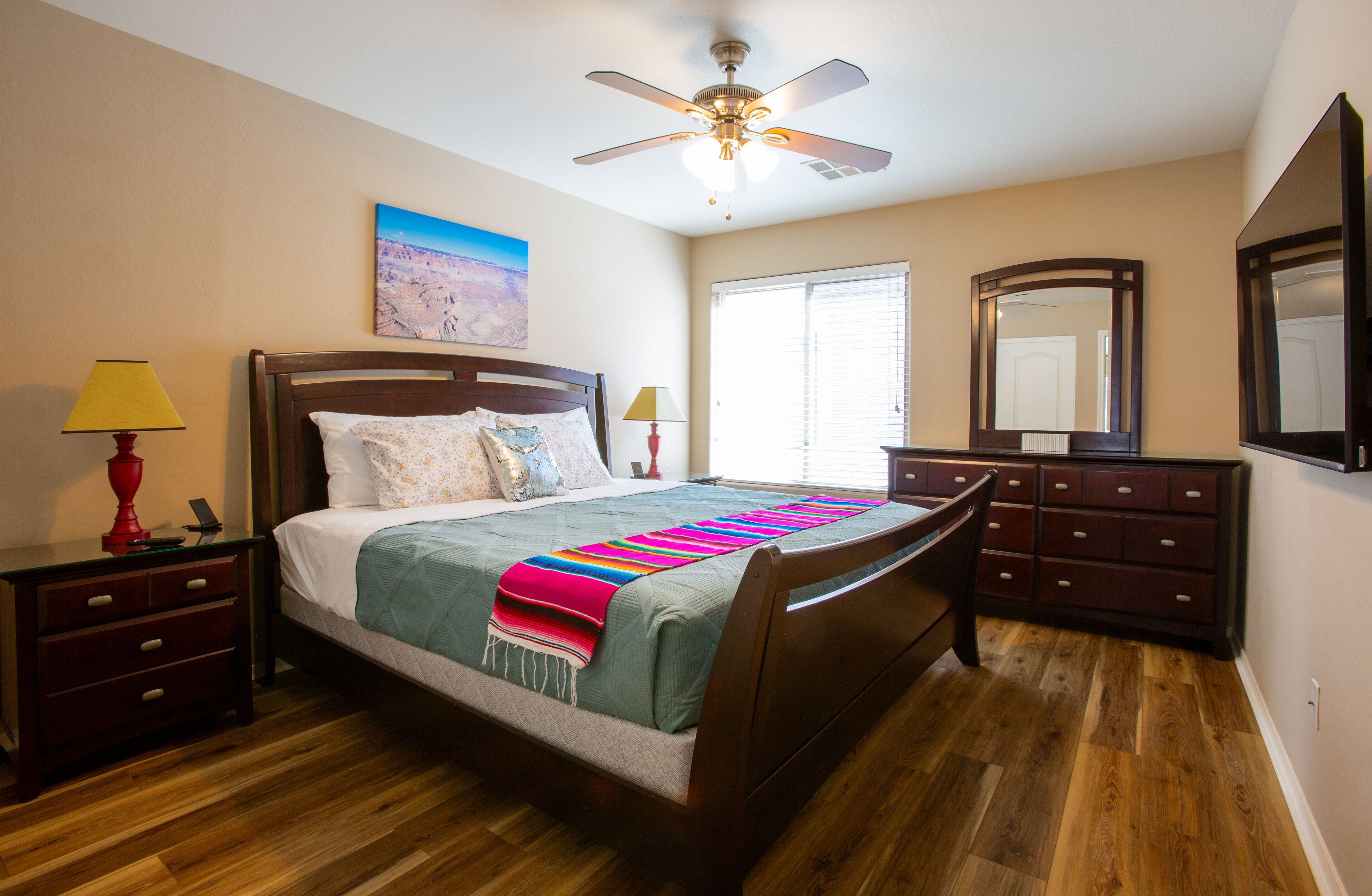 A bedroom with a bed, bedside tables, a ceiling fan, a window, a dresser, and a mirror.