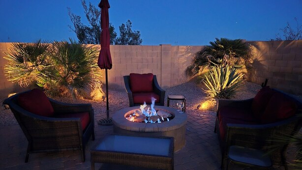 An outdoor patio area with a fire pit, wicker furniture, and ambient lighting. - Newly Remodeled Beautiful Home and Large Sparkling Pool, New Hot Tub & Game Room (San Tan Valley)