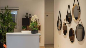 A reception area with a white counter, potted plants, and a wall with multiple mirrors.