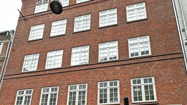 Un edificio de ladrillo de varios pisos con una entrada central, numerosas ventanas y un letrero sobre la entrada.