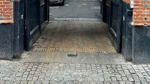 Un arco de ladrillo que da a un estrecho callejón, con un coche aparcado y un edificio al fondo.