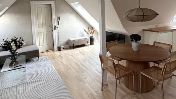 A spacious loft with a high ceiling, a dining area with a round table and chairs, a built-in bench, and a skylight. - Løvstræde baghus 4 th top floor (København)