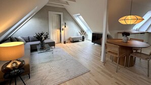 A spacious loft apartment with a high ceiling, a cozy seating area with a sofa and armchairs, a dining table with chairs, and a large window providing natural light. - Løvstræde baghus 4 th top floor (København)
