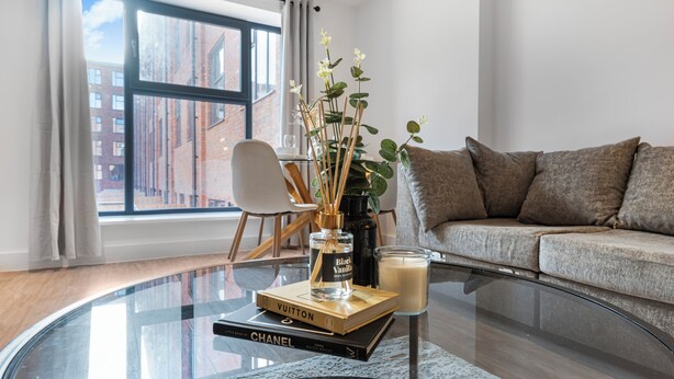 A modern living room with a glass coffee table, a sofa, and a view of a cityscape through large windows.